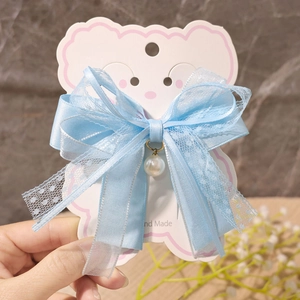 Detailed macro view of a light blue lace bow hair clip with white faux pearl pendant