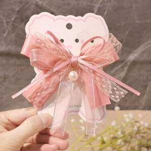 Detailed view of pink lace bow hair clip with pearl pendant on cloud display card