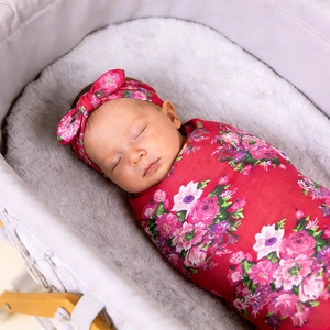 Ensemble lange floral pour bébé et bandeau à nœud assorti présenté dans un berceau