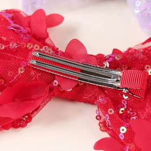 Macro view of red sequin bow hair clip showing secure metal alligator clip and ribbon wrap