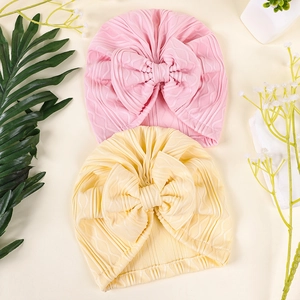 Close-up of baby knit hats with wavy texture and large bow in pink and yellow