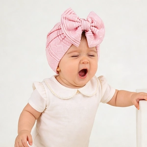 Close-up of soft pink knitted newborn beanie with large bow and wave texture