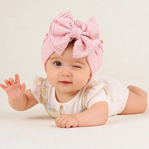Close-up of pink newborn turban with large bow detail on textured knit fabric