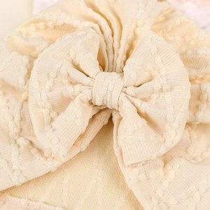 Détail macro du turban beige pour bébé en maille texturée douce avec un grand nœud