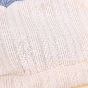 Vue macro du tissu en maille blanc crème avec texture chevron verticale sur le bonnet bébé