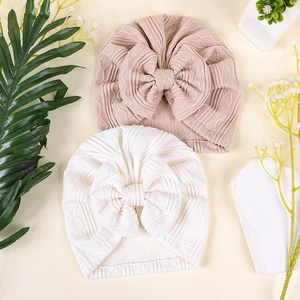 Detailed view of two knit newborn turbans with big bows in white and beige colors