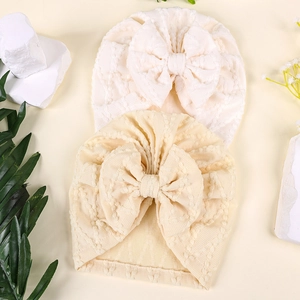 Détail de bonnets turban bébé avec nœud en blanc et beige au tricot gaufré