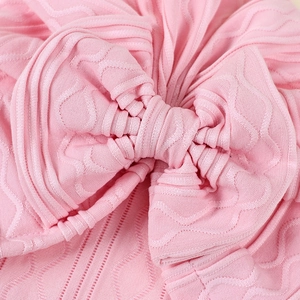 Macro shot of light pink baby bonnet with knit bow detail and soft jacquard wavy texture