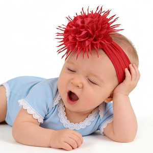 Détail du bandeau à grosse fleur rouge sur un bébé en barboteuse bleue avec dentelle