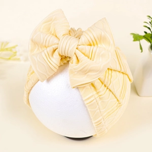 Detail of light yellow baby hat with large bow and wavy ribbed knit texture