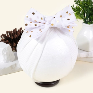 Detail eines Baby-Turbans in Weiß mit goldener gepunkteter Schleife und Rippstoff