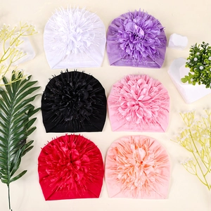 Flat lay of baby turban hats with large fabric flowers and feathers in six vibrant colors