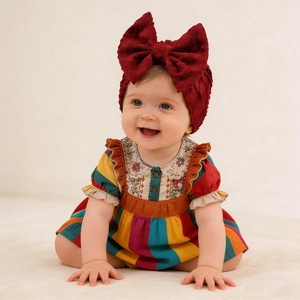 Détail d'une robe rayée pour bébé avec col fleuri et bandeau à gros nœud rouge foncé