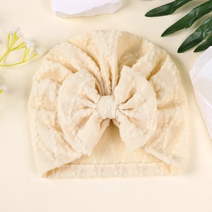 Gros plan sur le bonnet turban bébé beige avec texture gaufrée et nœud surdimensionné