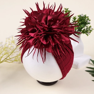 Detail eines weinroten Baby-Turbans mit großer Camellia-Blüte und glänzenden Strasssteinen