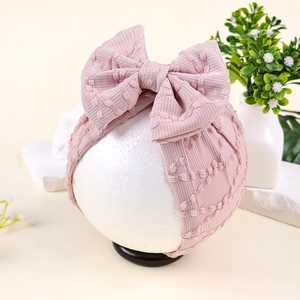 Détail d'un turban en tricot rose pour bébé avec un grand nœud sur tête de mannequin