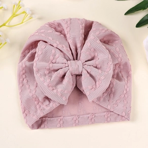 Gros plan du bonnet turban rose pour bébé avec gros nœud et texture en maille douce