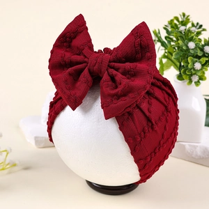 Détail du turban bébé rouge foncé avec un grand nœud texturé présenté sur un mannequin
