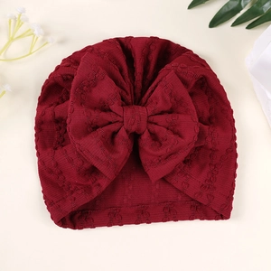 Détail du bonnet turban pour bébé avec un grand nœud bordeaux et une texture jacquard