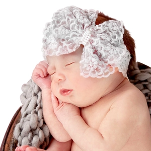 Bandeau bébé en dentelle blanche avec nœud et perle porté par un nouveau-né