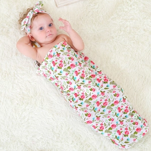 Detailed view of floral baby swaddle wrap and matching bow headband on white plush rug