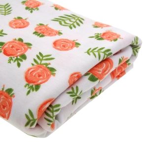 Close-up detail of soft white cotton baby swaddle with orange rose floral patterns
