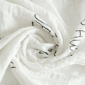 Close-up of soft white muslin swaddle blanket with black artistic letter print