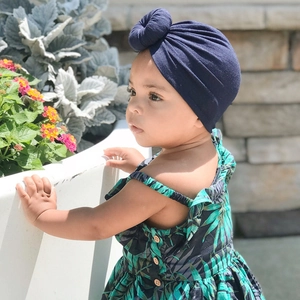 Detail of dark blue baby turban with top knot and tropical print cotton romper