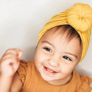 Detailed view of baby girl wearing bright yellow turban hat with a ribbed top knot ball