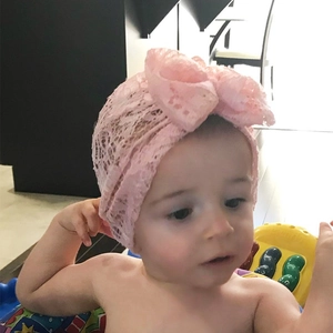 Detailed view of an infant girl wearing a light pink lace headband with a large bow