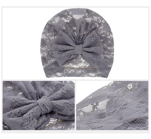 Detailed close-up of grey lace baby hat with floral patterns and a large bow decoration