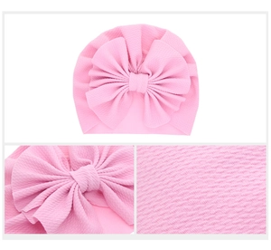 Pink infant turban hat detail with large bow and textured waffle fabric close-up
