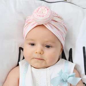 Close-up of pink and white striped knit baby donut hat with a top knot design