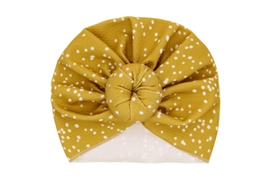 Close-up of mustard yellow polka dot baby turban hat with a circular donut knot detail