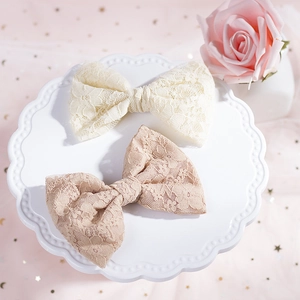 Vista dettagliata di due fermagli per capelli a farfalla in pizzo beige e rosa su supporto