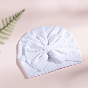 Detailed close-up of a white cotton ribbed baby turban hat with a large decorative bow