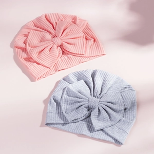 Detailed view of two ribbed knit baby turban hats in pink and grey with large bows