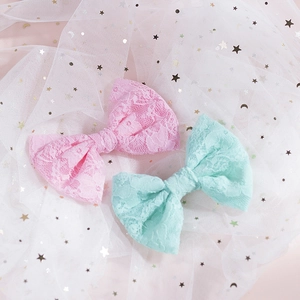 Dettaglio di fermagli a fiocco in pizzo rosa e verde menta su sfondo di tulle con stelle e lune