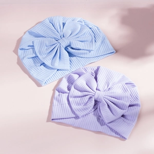 Close-up of baby turban hats with large bows in light blue and purple ribbed knit fabric