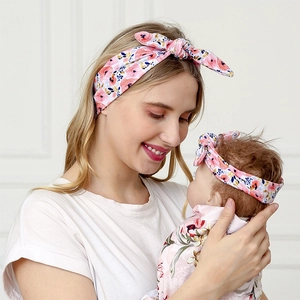 Close-up of mother and baby wearing matching floral bunny ear headbands in a warm setting