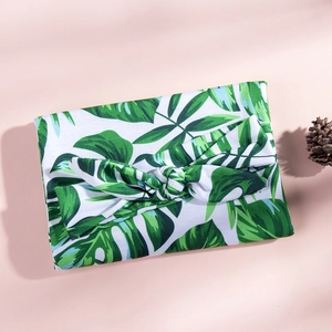Detail of baby swaddle blanket and matching bow headband with green tropical leaf prints