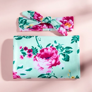 Close-up of mint floral baby swaddle blanket set with matching bow headband on pink background