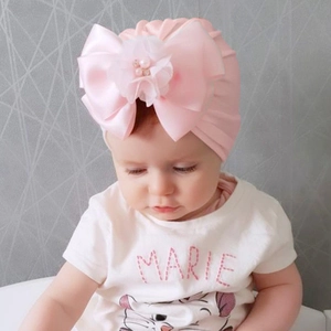 Dettaglio del turbante rosa per neonata con grande fiocco in raso e fiori di perle