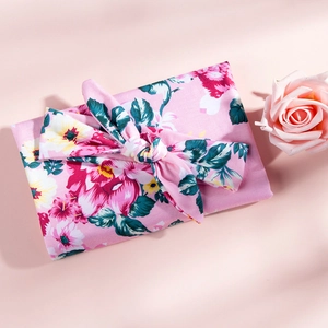 Floral baby swaddle and matching bow headband set for newborns on a soft pink background