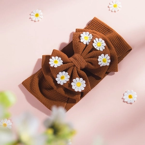 Détail d'un bandeau bébé en tricot gaufré marron avec broderie de fleurs de marguerite