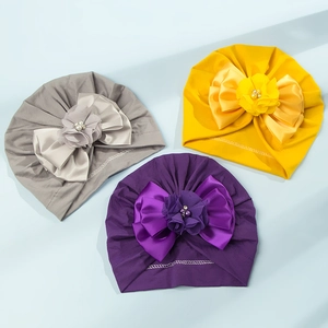 Dettaglio di turbanti neonato grigio, giallo e viola con fiocco e fiore con perle fini