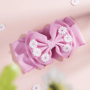 Détail du bandeau bébé rose avec grand nœud et broderies de fleurs de marguerites