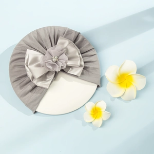 Dettaglio di un turbante per neonati con grande fiocco in raso e fiori 3D con perle