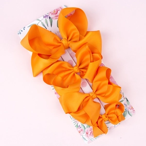 Set of four orange grosgrain ribbon bow hair clips on floral display card