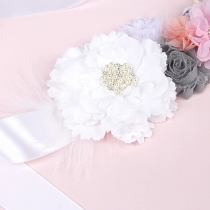 Detail of baby shower sash with white fabric flower, pearls, and soft pink feathers
